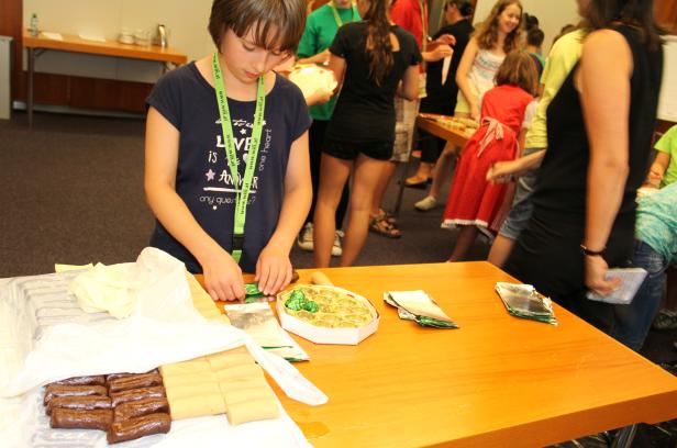 Ein Mädchen verpackt Pralinen an einem Tisch, an dem sich weitere Personen bedienen.