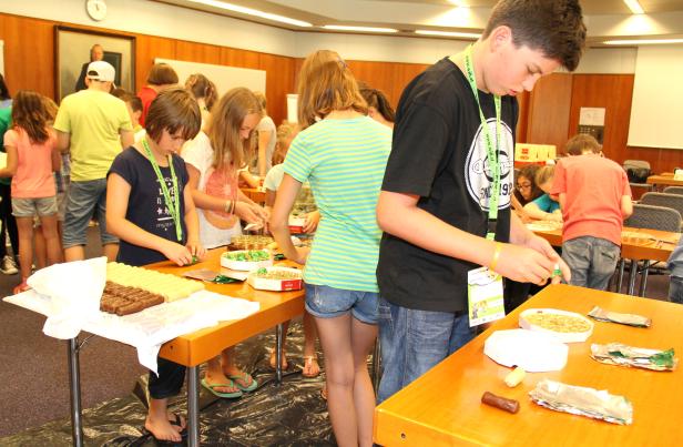 Eine Gruppe Kinder bastelt und verpackt Süßigkeiten an mehreren Tischen.