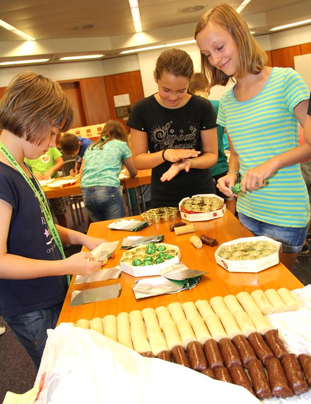 Mehrere Kinder verpacken Marzipan und Pralinen an einem Tisch.