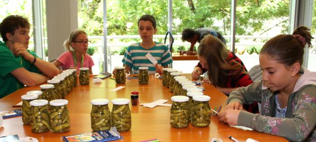 Eine Gruppe Kinder sitzt an einem Tisch und bastelt mit Gurkengläsern.