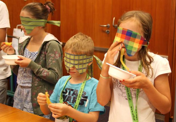 Kinder mit verbundenen Augen essen Gurken bei einem Geschmacks-Test.