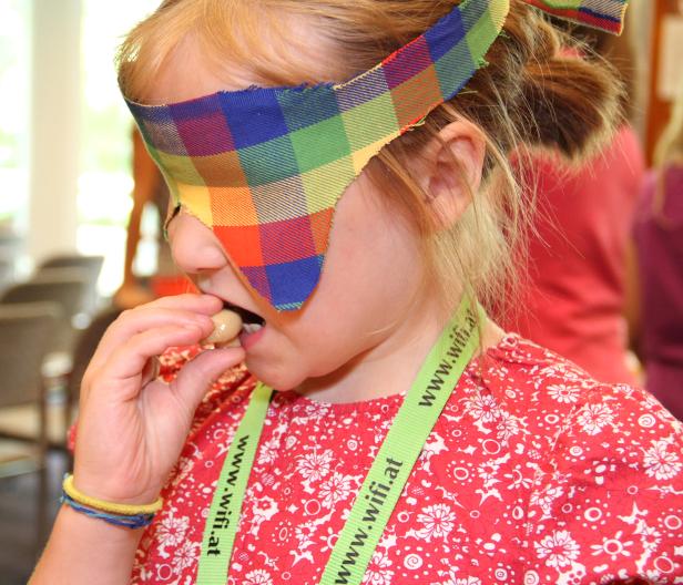 Ein Mädchen mit einer bunten Augenbinde isst eine Süßigkeit.