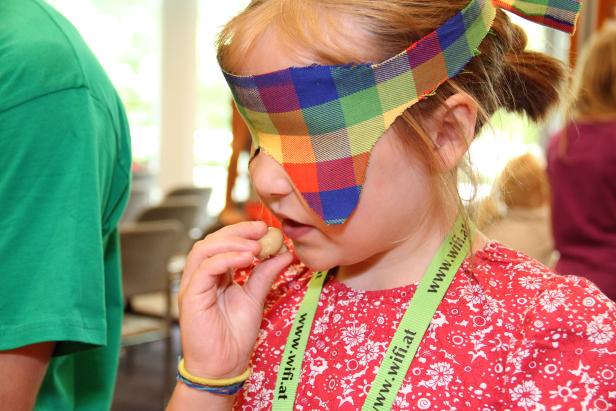 Ein Mädchen mit Augenbinde isst eine Kartoffel.