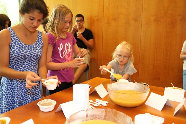 Mehrere Kinder probieren eine gelbe Suppe an einem Tisch.