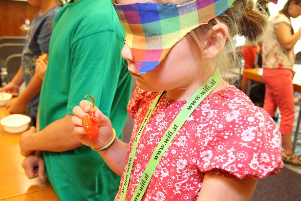 Ein Kind mit Augenbinde hält eine orangefarbene Süßigkeit in der Hand.