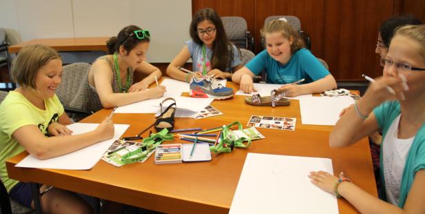 Eine Gruppe Mädchen sitzt an einem Tisch und zeichnet Schuhe.