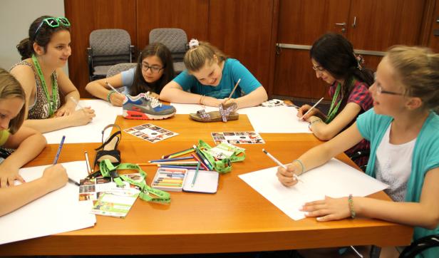 Eine Gruppe von Mädchen sitzt an einem Tisch und zeichnet Schuhe.