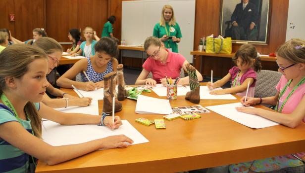 Mehrere Mädchen sitzen an einem Tisch und zeichnen mit Bleistiften auf Papier.