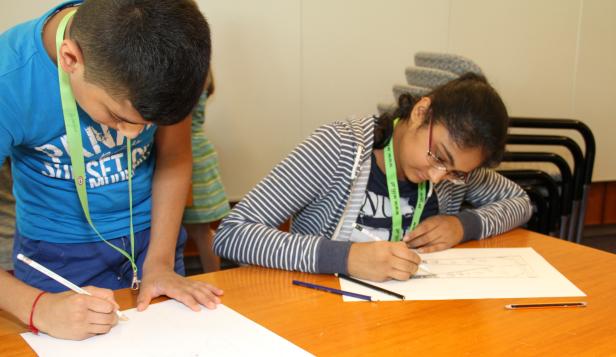 Zwei Kinder sitzen an einem Tisch und zeichnen mit Bleistiften auf Papier.