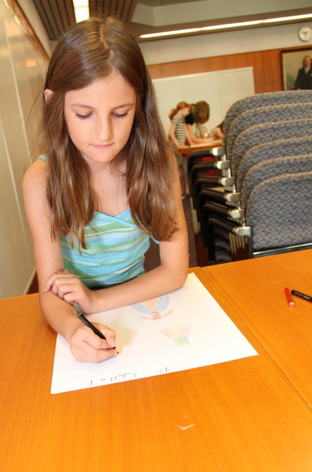 Ein Mädchen zeichnet auf einem Blatt Papier auf einem Tisch.