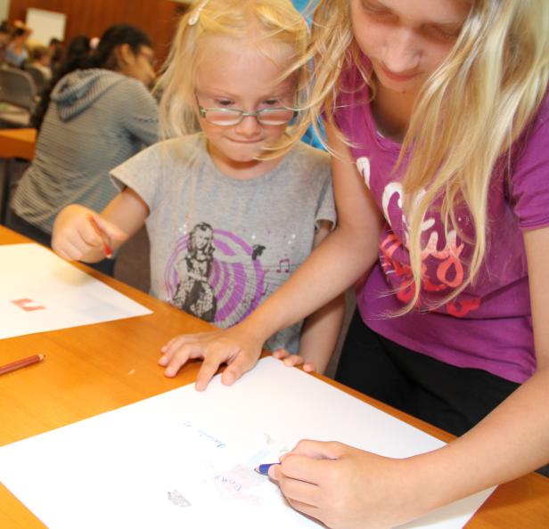 Zwei Mädchen sitzen an einem Tisch und malen mit Buntstiften auf Papier.