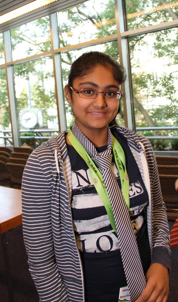 Eine junge Frau mit Brille und gestreifter Jacke lächelt in die Kamera.