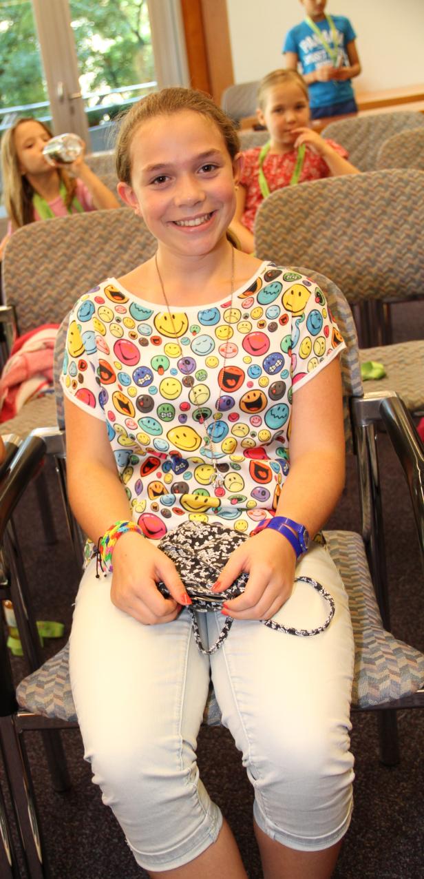 Ein lächelndes Mädchen sitzt mit einer kleinen Handtasche auf einem Stuhl.