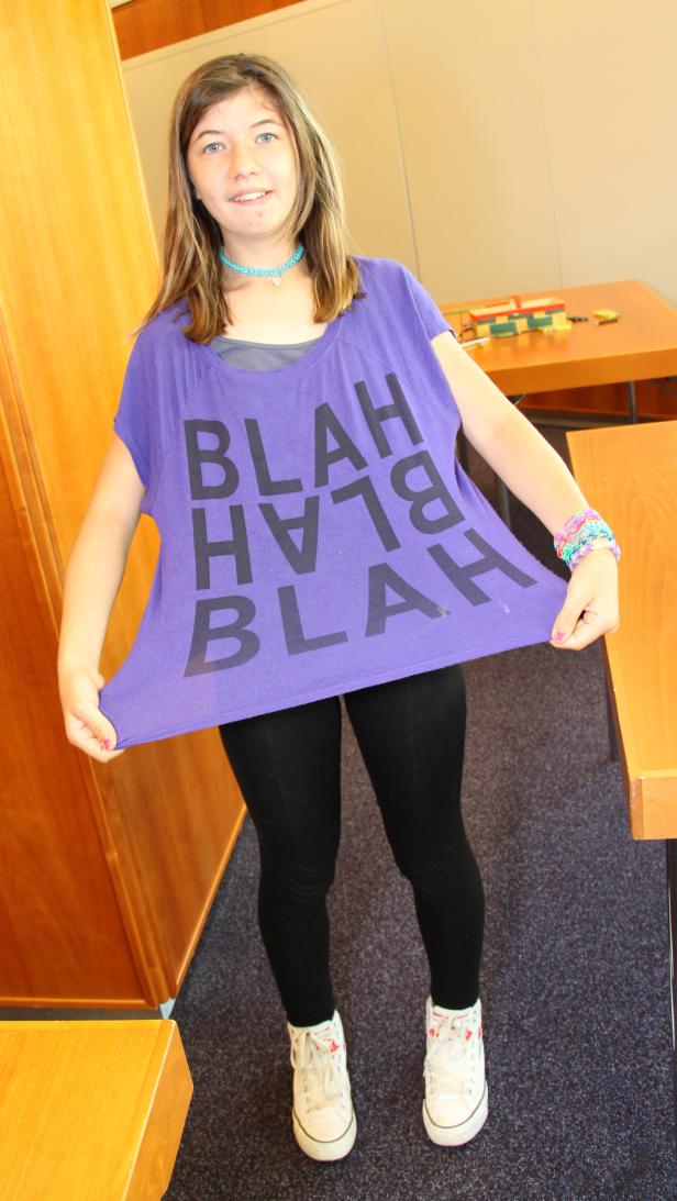 Ein junges Mädchen zeigt ein lila T-Shirt mit der Aufschrift „Blah“.