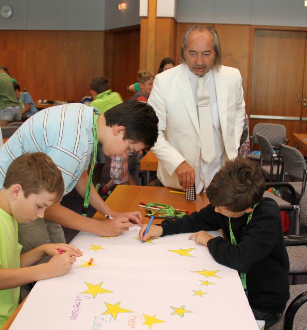 Kinder malen mit einem Mann im weißen Anzug eine Europaflagge.