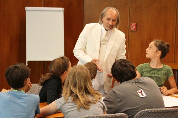 Ein Mann in einem weißen Anzug spricht vor einer Gruppe von Kindern.
