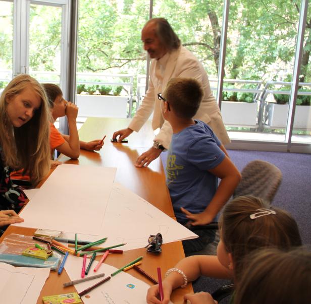Eine Gruppe Kinder sitzt mit einem Mann an einem Tisch und zeichnet.