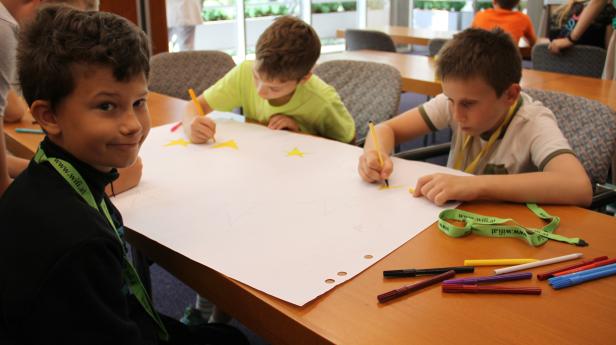 Drei Jungen malen gelbe Sterne auf ein großes Blatt Papier.