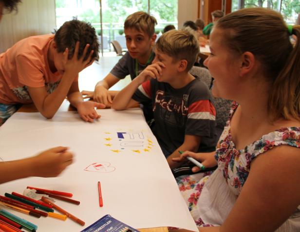 Eine Gruppe Kinder sitzt an einem Tisch und malt mit Stiften ein Bild der EU-Flagge.