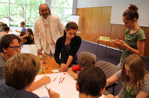 Eine Gruppe von Kindern sitzt mit einem Mann an einem Tisch und zeichnet.