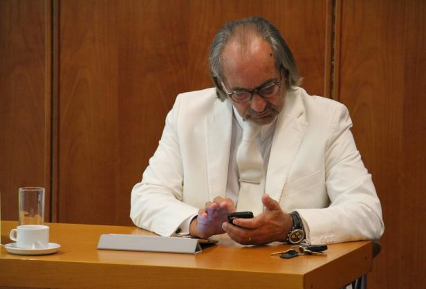 Ein Mann im weißen Anzug sitzt am Tisch und tippt auf seinem Smartphone.