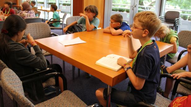 Eine Gruppe Kinder sitzt an einem Tisch und liest oder denkt nach.