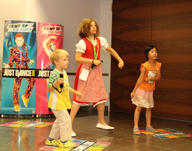 Drei Kinder tanzen vor Postern für das Spiel „Just Dance“.
