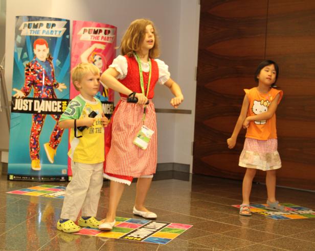 Drei Kinder tanzen vor Postern für das Spiel „Just Dance“.