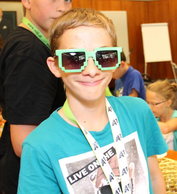 Ein lächelnder Junge mit pixeliger, grüner Sonnenbrille und einem A1-Lanyard um den Hals.