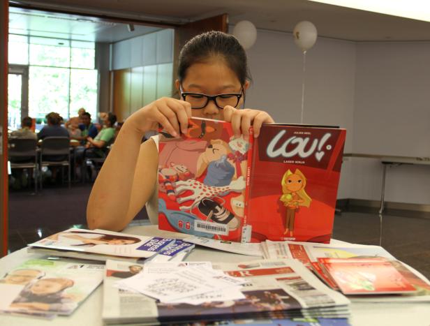 Ein Mädchen mit Brille liest die Comicreihe „Lou! Laser Ninja“ von Julien Neel.