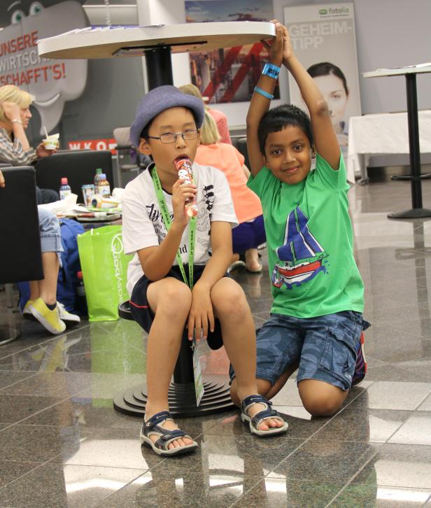 Zwei Jungen sitzen unter einem Tisch, einer isst ein Eis.