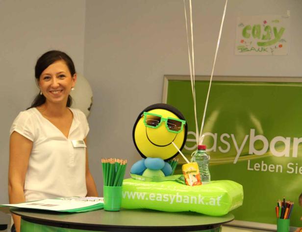Eine freundliche Easybank-Mitarbeiterin steht an einem Stand mit einem Maskottchen und Werbematerialien.