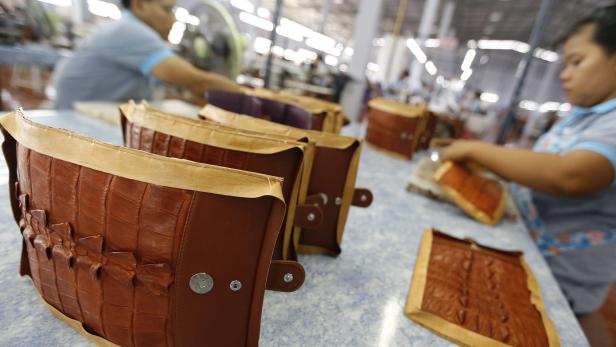 In einer Fabrik werden braune Handtaschen aus Krokodilleder hergestellt.