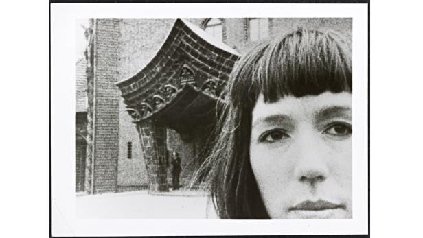 Das Gesicht einer Frau vor einem Gebäude mit einem verzierten Eingangsbereich.