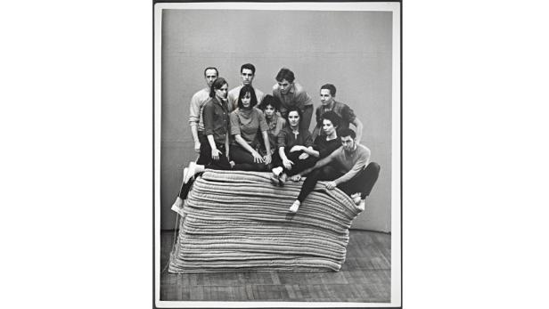 Eine Gruppe von zehn Personen sitzt und steht auf einem Stapel von Matratzen.