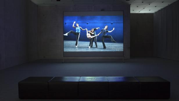 In einem Ausstellungsraum wird ein Video von drei Tänzerinnen auf einer Leinwand gezeigt.