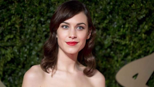 Alexa Chung mit rotem Lippenstift vor einem grünen Hintergrund.