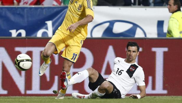 Ein Fußballspieler liegt auf dem Rasen, während ein anderer den Ball tritt.