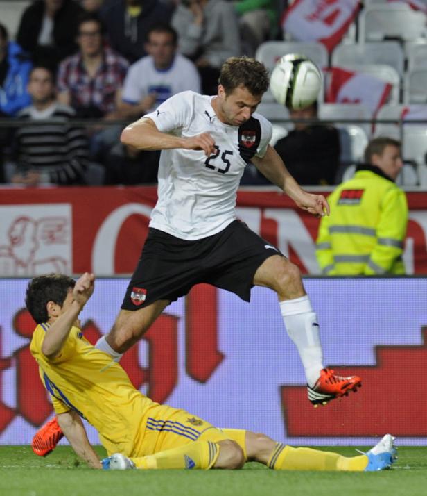 Ein österreichischer Fußballspieler springt über einen am Boden liegenden ukrainischen Spieler.