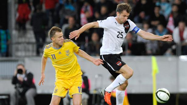 Ein österreichischer Fußballspieler springt, um den Ball vor einem ukrainischen Spieler zu erreichen.