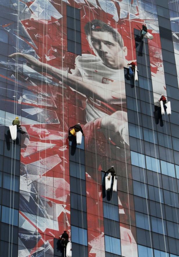 Fensterputzer arbeiten an einem Gebäude mit einem großen Porträt von Robert Lewandowski.