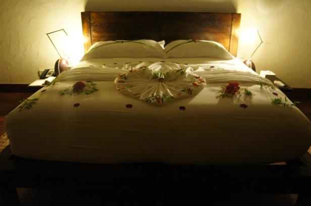 Ein dekoriertes Bett mit einem gefalteten Handtuchherz und Blütenblättern in einem Hotelzimmer.