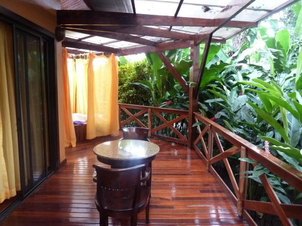 Ein Tisch und Stühle stehen auf einer Holzterrasse mit Blick auf üppige tropische Vegetation.