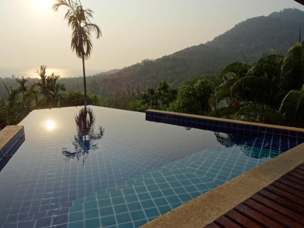 Ein Infinity-Pool mit Blick auf eine tropische Landschaft bei Sonnenuntergang.