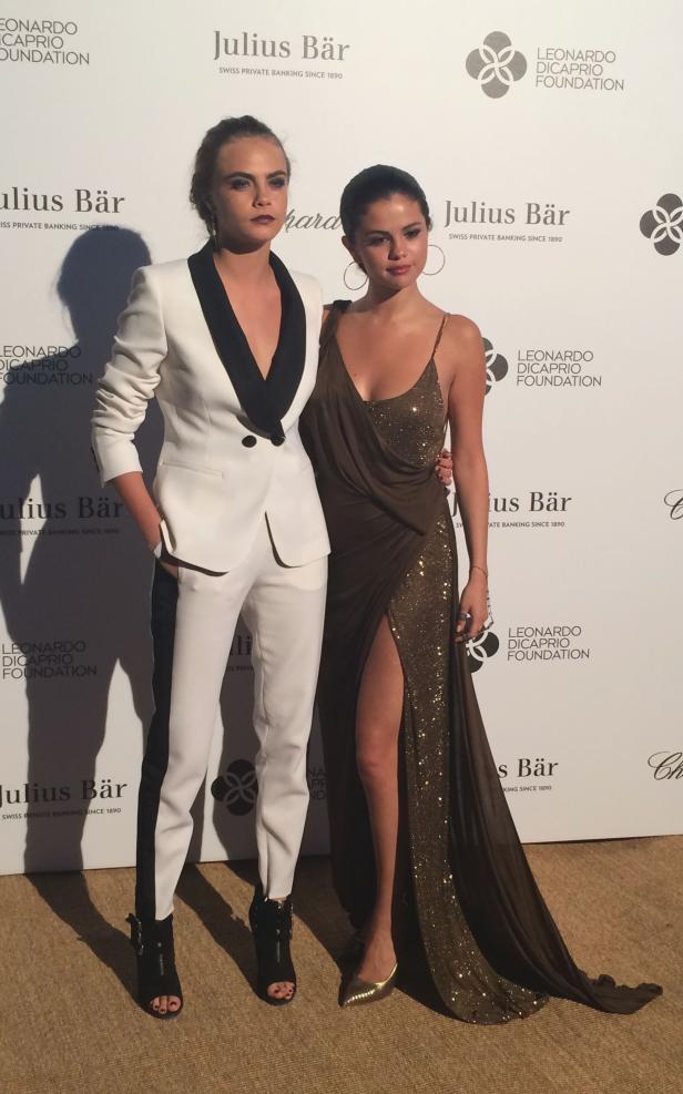 Cara Delevingne und Selena Gomez posieren auf einem Event vor Sponsorenlogos.