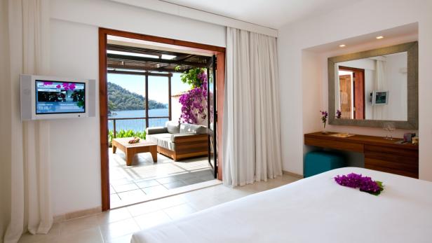 Ein helles Hotelzimmer mit Zugang zu einer Terrasse mit Meerblick.