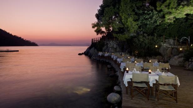 Ein gedeckter Tisch am Ufer mit Blick auf das ruhige Wasser bei Sonnenuntergang.