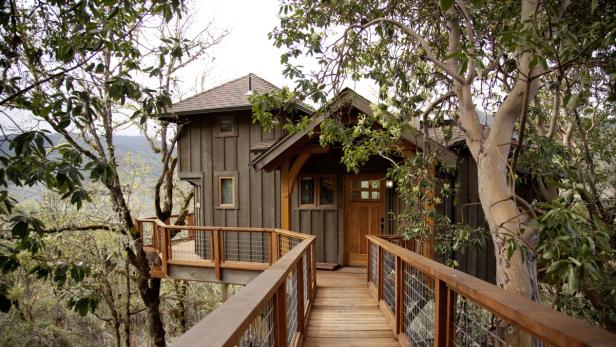 Ein Holzhaus, das auf Stelzen zwischen Bäumen steht.