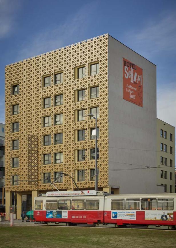 Ein modernes Hotelgebäude mit einer Fassade aus einem Lochmuster und eine rote Straßenbahn davor.
