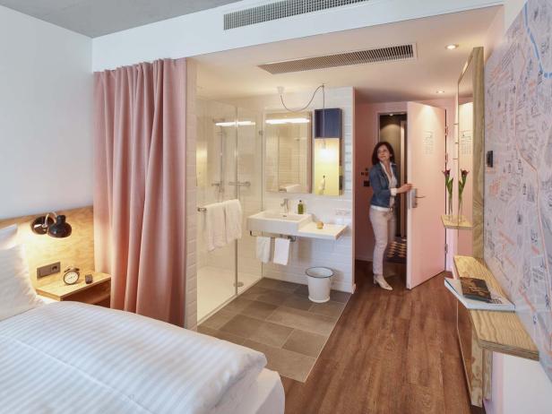 Eine Frau betritt ein Hotelzimmer mit Bett und offenem Badezimmer.